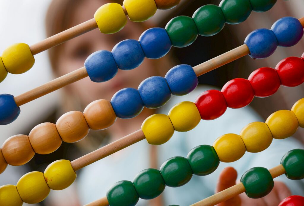 Close-up of colorful wooden abacus with a child learning math in the background, focusing on education and early childhood development.