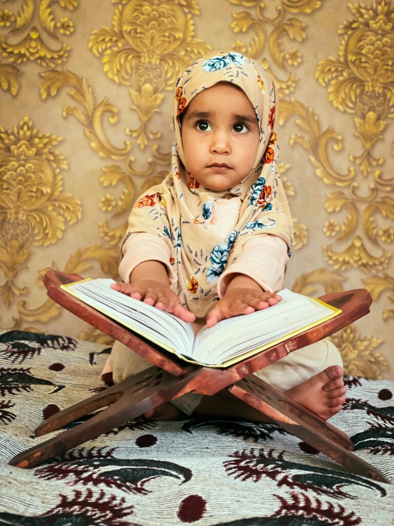 Little girl in hijab reading Quran indoors, embracing Islamic culture.